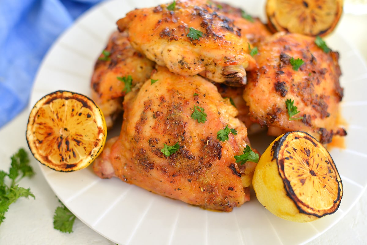 close up of chicken thighs on a plate with charred lemons 