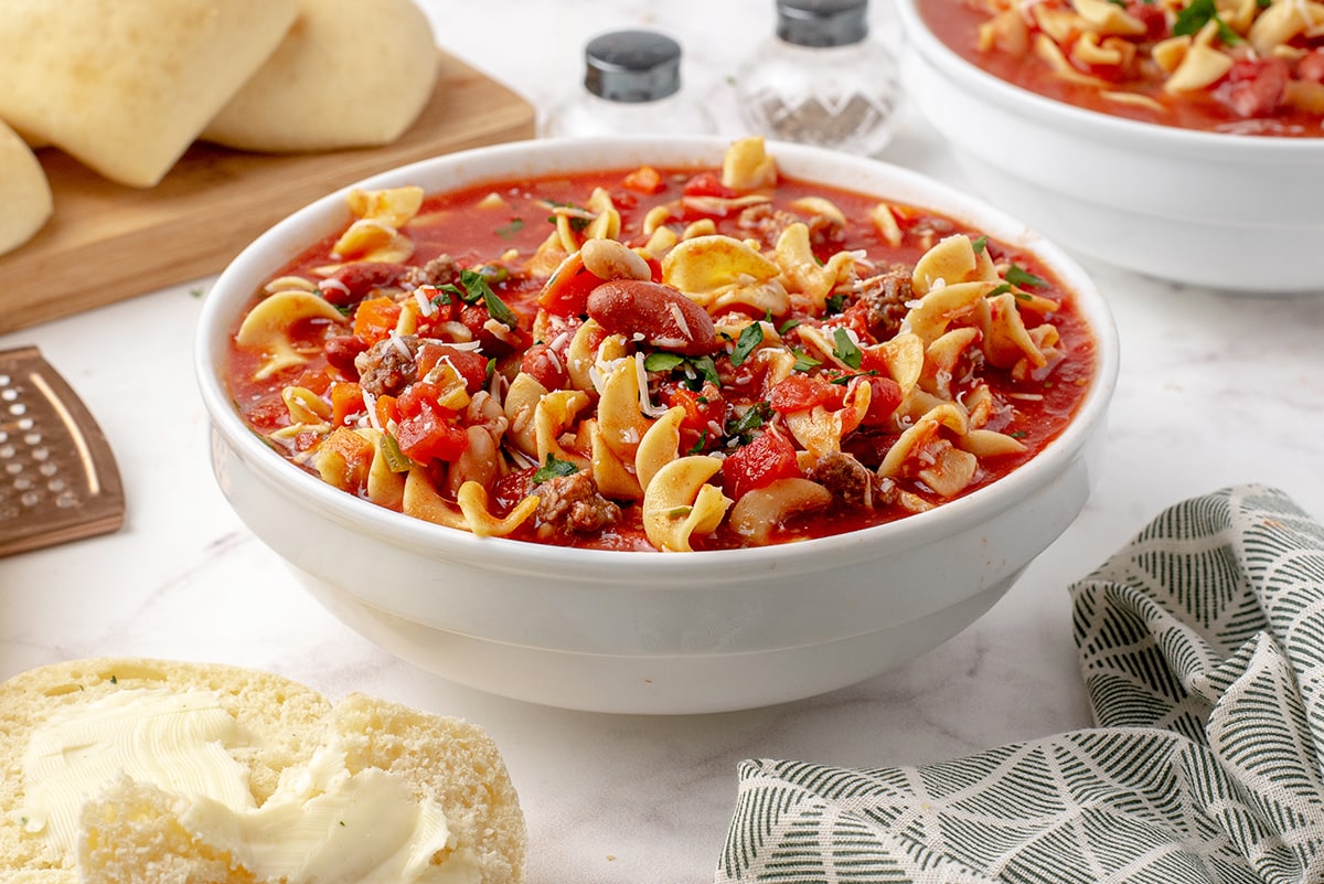 white soup bowl of pasta e fagioli soup with bread in the background 