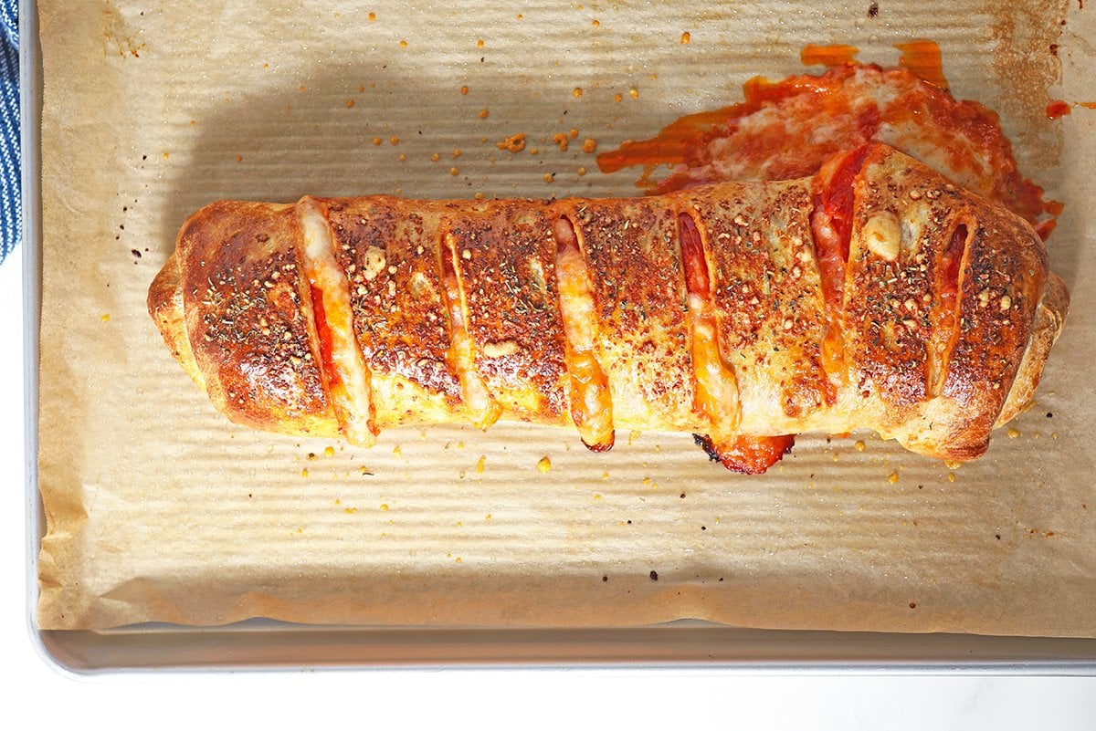 overhead of pepperoni stromboli on a baking sheet with cheese oozing out the side 