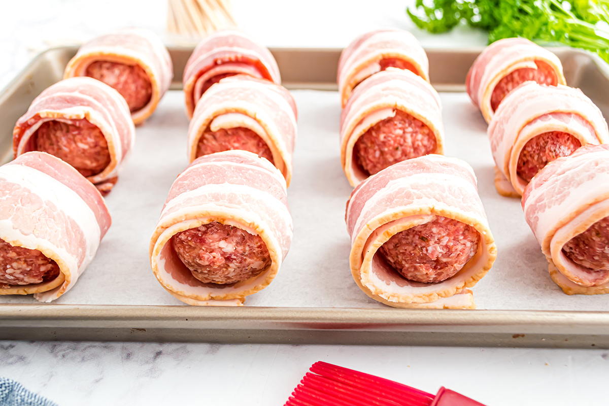 side view of bacon wrapped meatballs on a baking sheet 