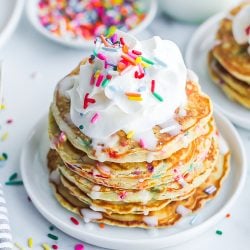 angle view of a stack of funfetti pancakes topped with whipped cream and sprinkles