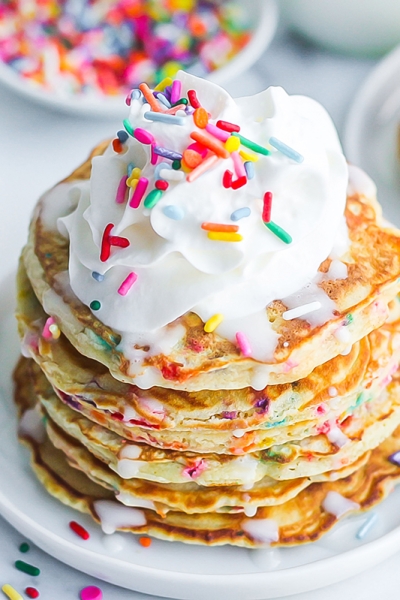 angle view of a stack of funfetti pancakes topped with whipped cream and sprinkles