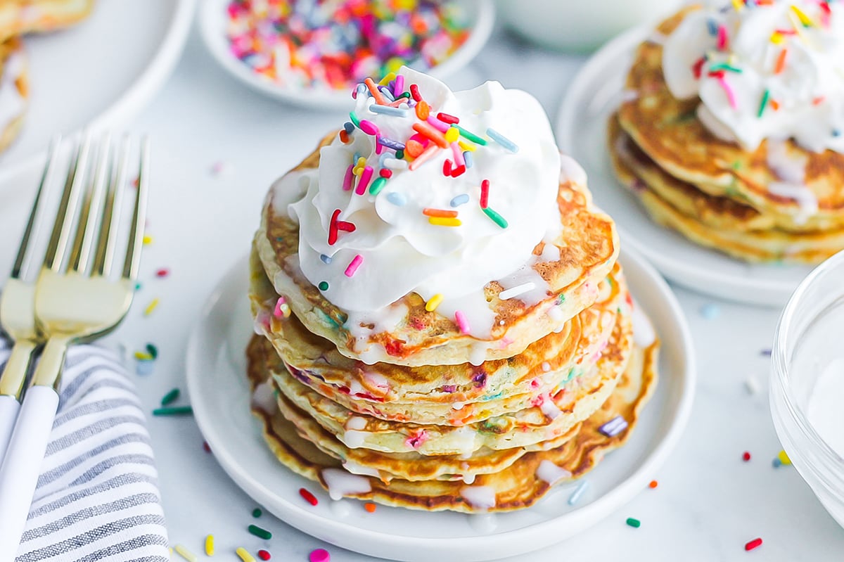 angle view of a stack of funfetti pancakes topped with whipped cream and sprinkles