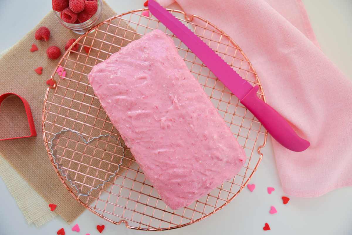 overhead of pink glazed pound cake on a copper wire rack 