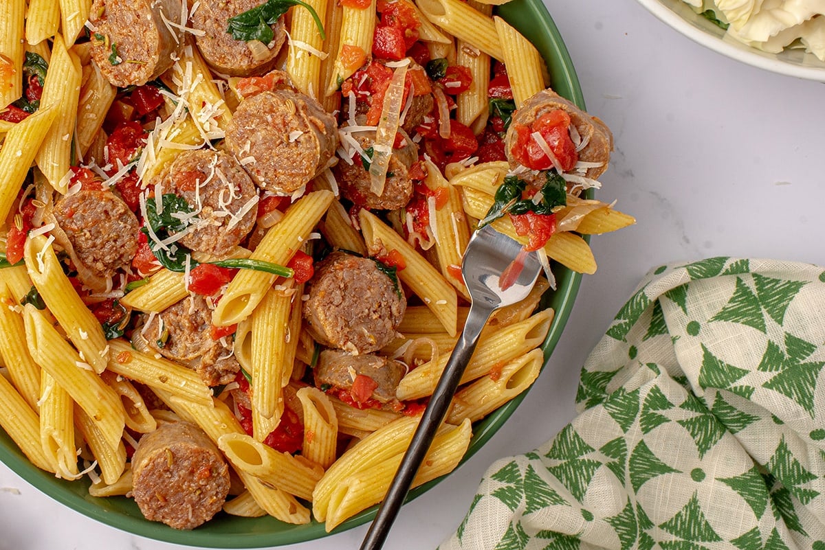 sausage pasta on a fork leaning on a green bowl 