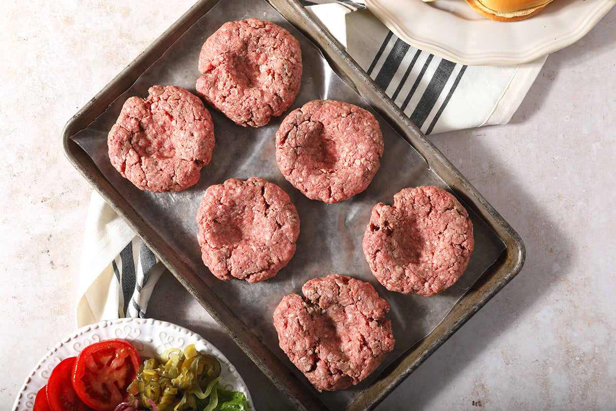 formed raw hamburger patties on a baking sheet 