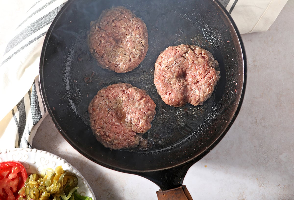 overhead of burger patties in a cast iron skillet 