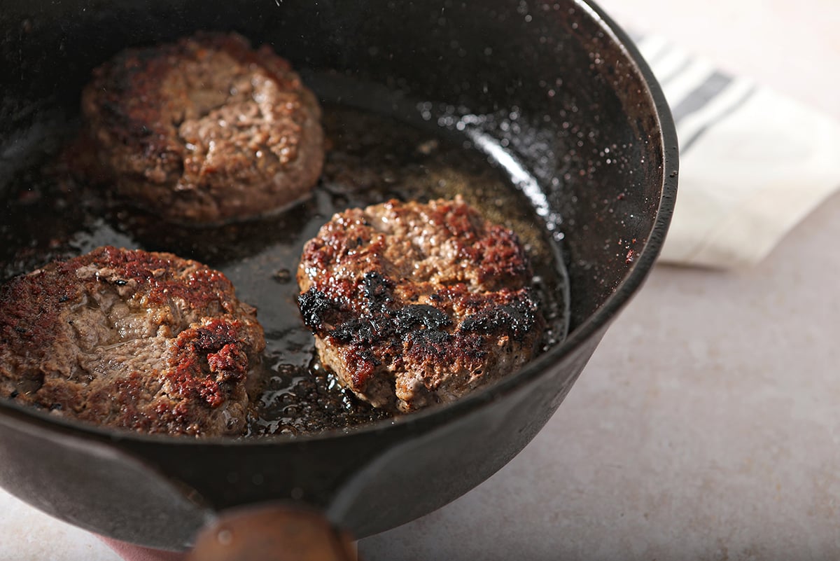 angle view of a browned burger patty in a cast iron skillet 