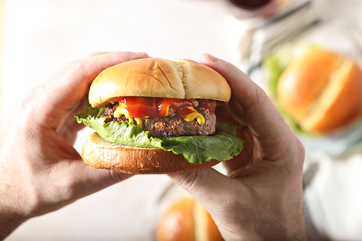 hands holding a hamburger with ketchup, mustard and lettuce