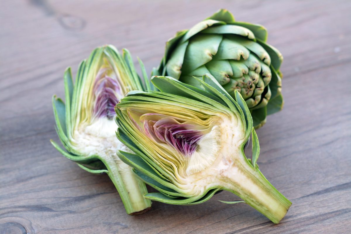 fresh artichoke cut in half on a cutting board 