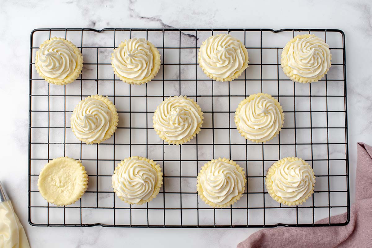 cupcakes topped with cream cheese frosting on a wire rack  