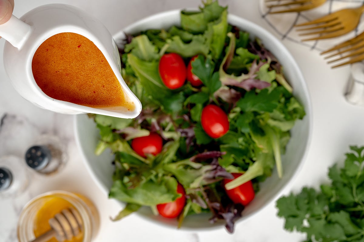 homemade salad dressing pouring over a leafy green salad 