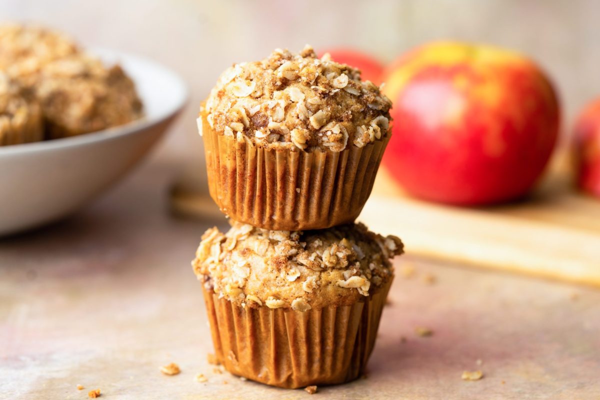 stack of apple sauce muffins with bowl of muffins and red apples in the background