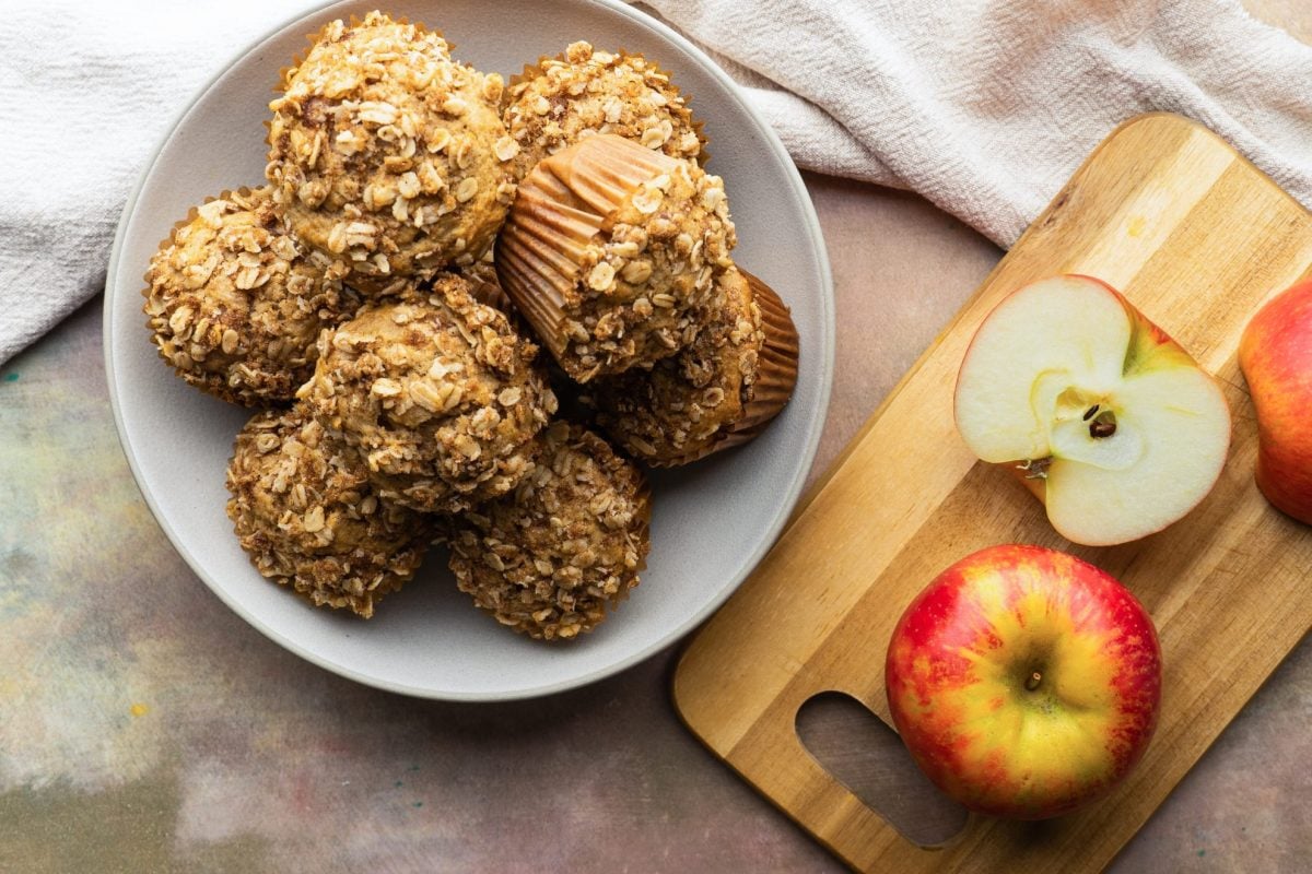 overhead shot of a bowl of applesauce muffins with a cut apple on a cutting board next to it