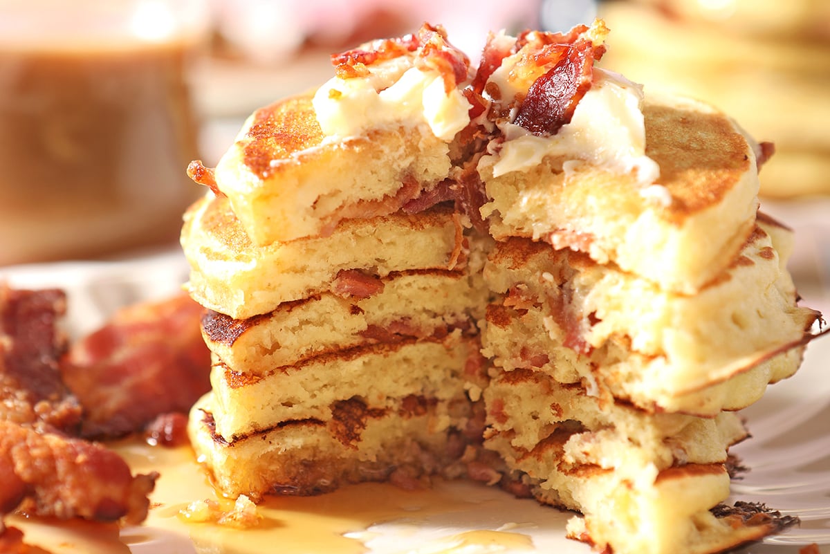 giant stack of pancakes with a section cut out and bacon and butter 