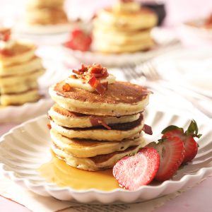 large stack of bacon pancakes with strawberry topping