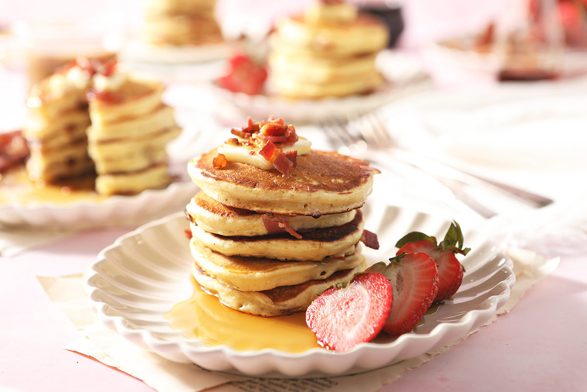 large stack of bacon pancakes with strawberry topping