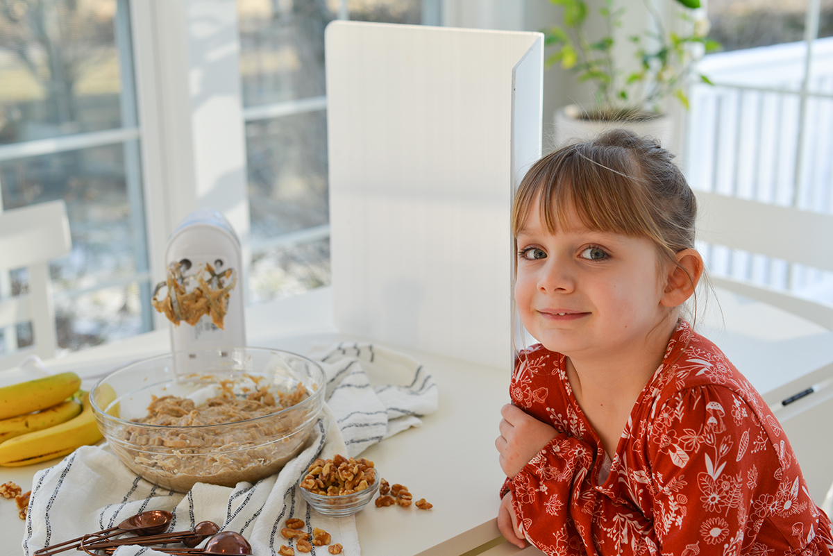 little girl sitting next to a table with muffin batter and a blender 