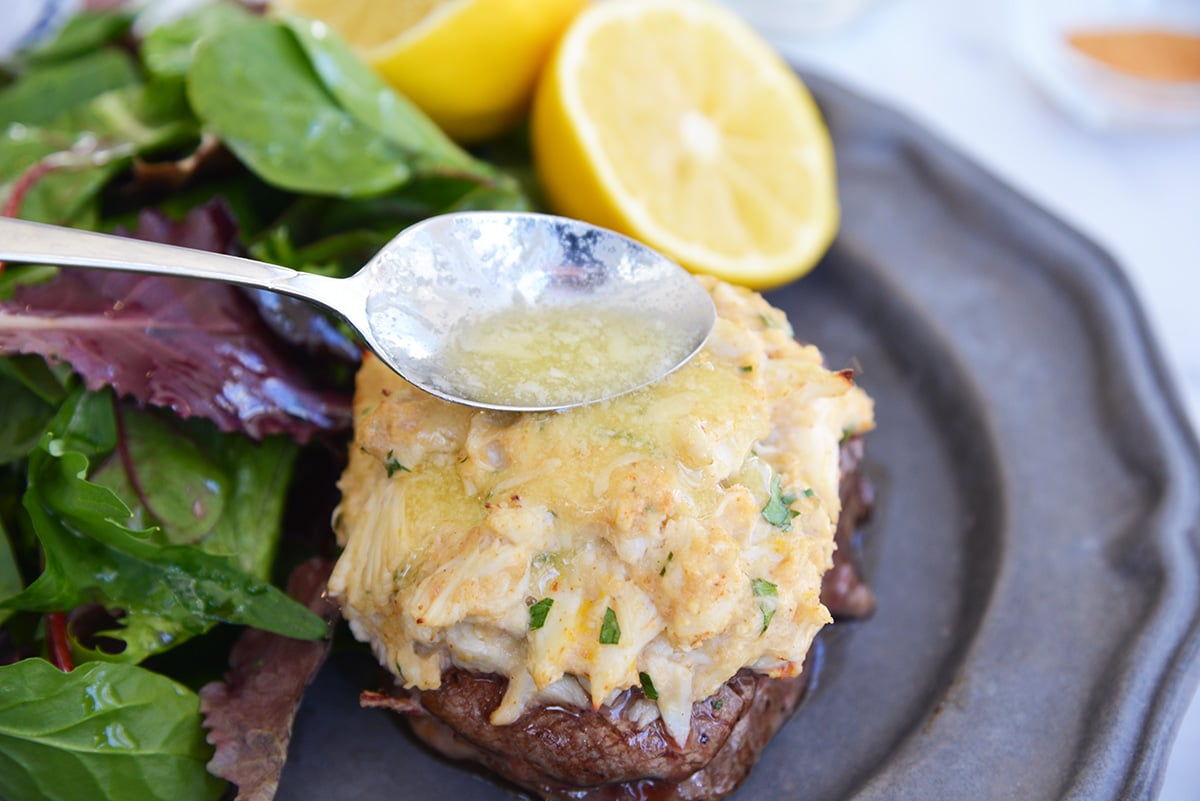 spooning butter sauce over a filet mignon with crab topping 