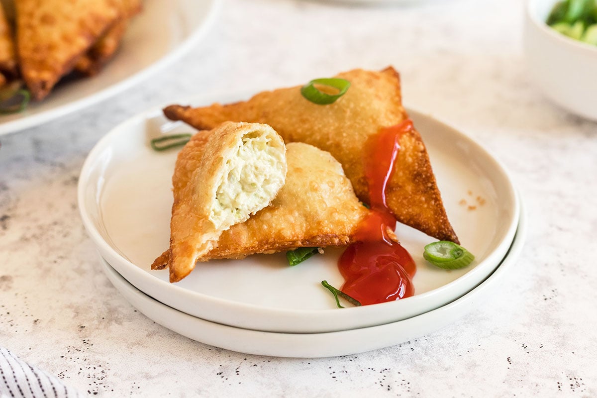 close up of crab rangoons on a small serving plate with sauce 