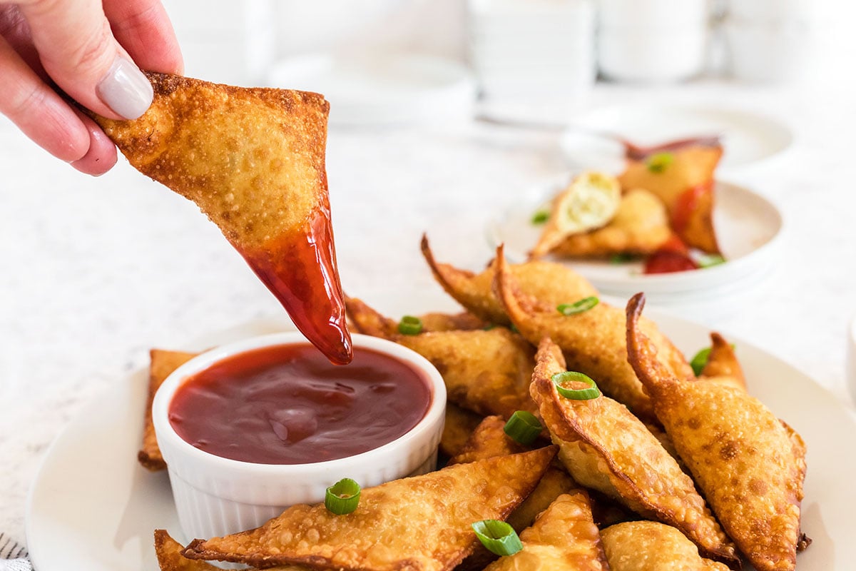 hand dipping a rangoon into sauce 