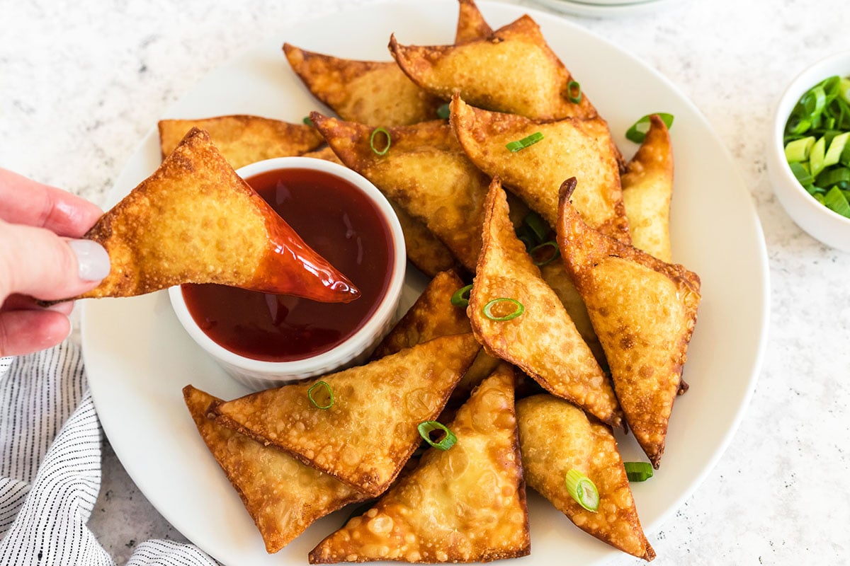 dipping a crispy rangoon in red sauce