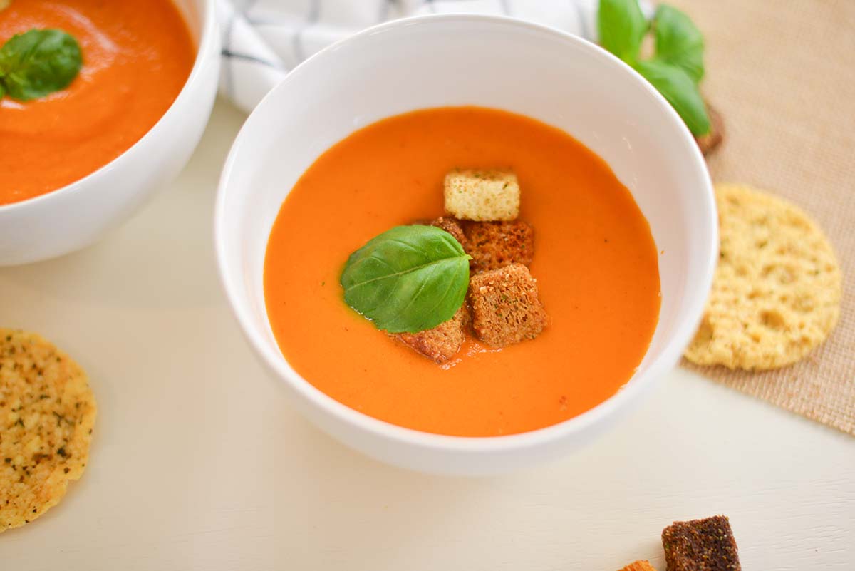 two bowls of tomato soup with croutons and basil leaves 