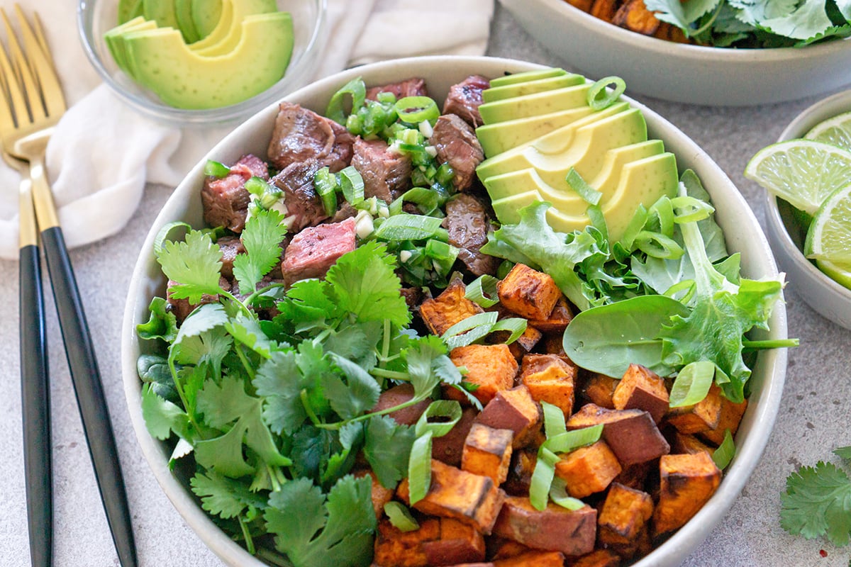 angle of steak bowl in a white serving bowl with fresh lime wedges 