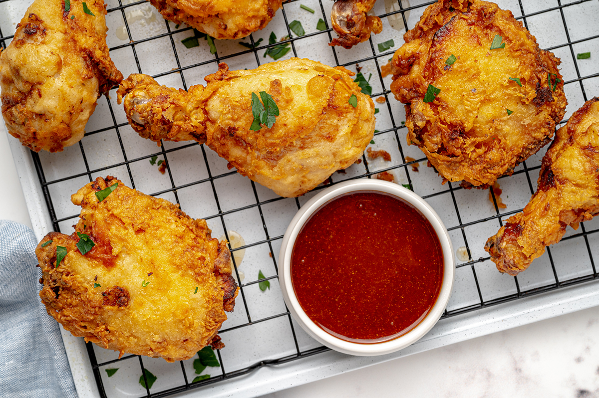 close up of buttermilk fried chicken on wire rack with hot sauce