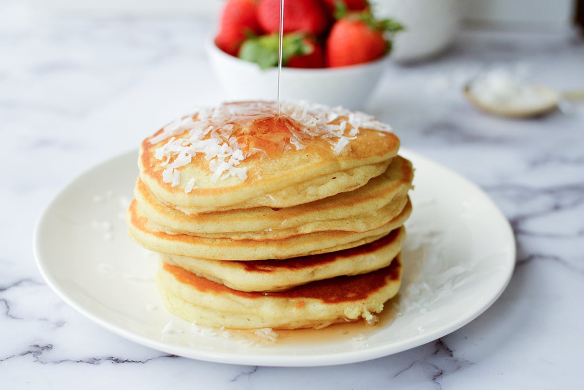 stack of coconut pancakes with syrup poured on top