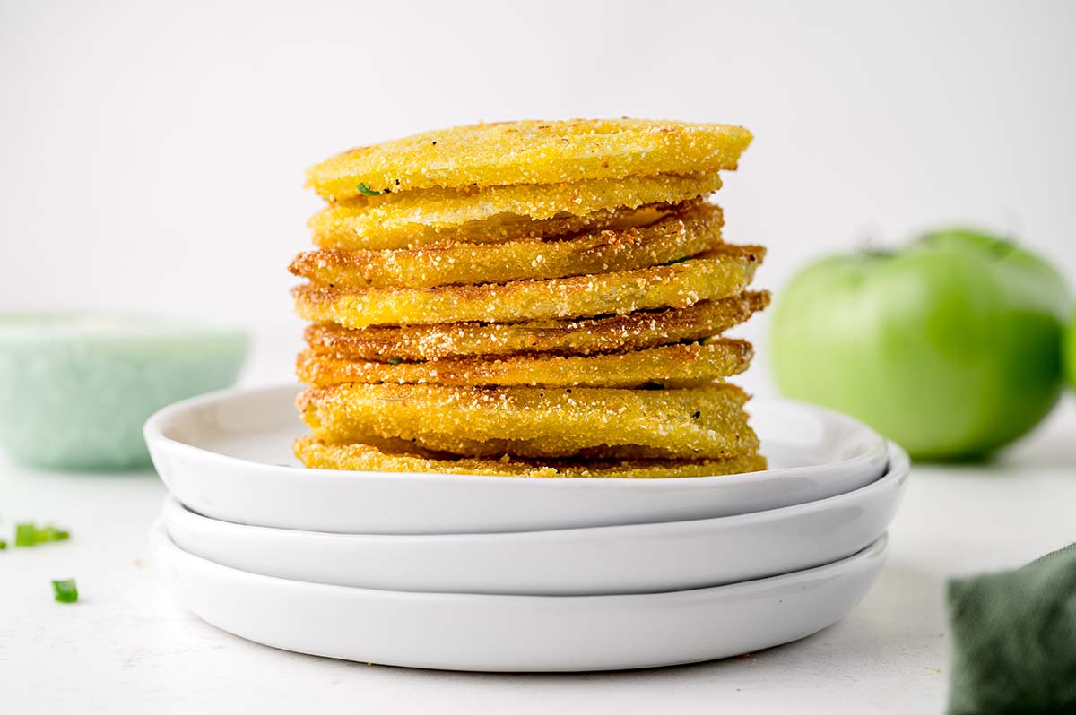 stack of green tomatoes fried in yellow cornmeal on white plates