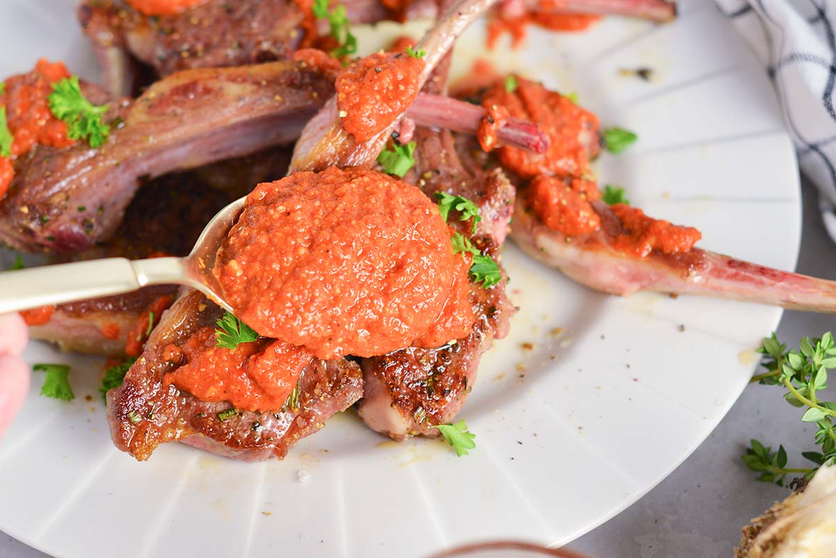 spooning romesco recipe over lamb chops