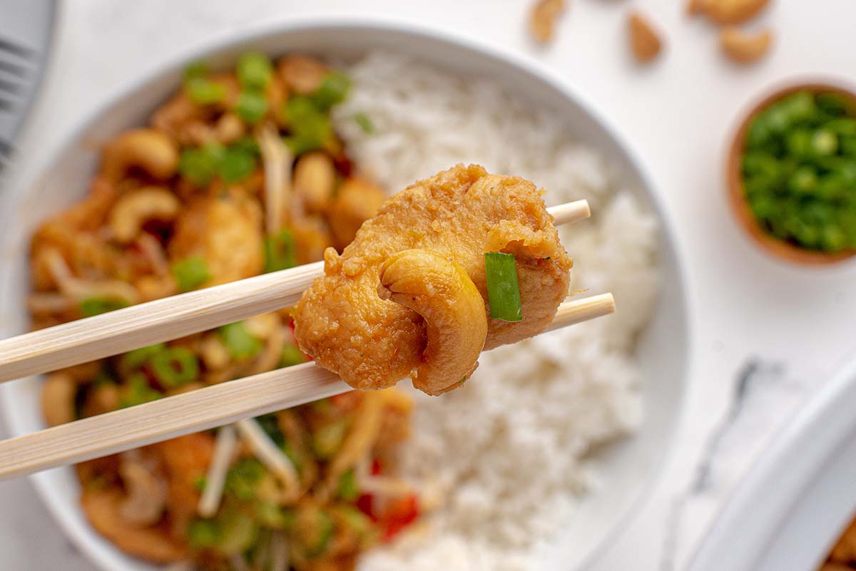 piece of chicken with a cashew on a chopstick 