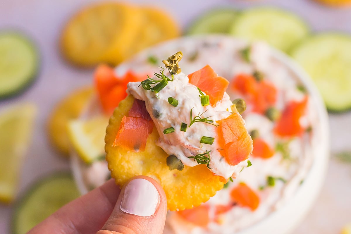 hand holding cracker dipped in smoked salmon dip