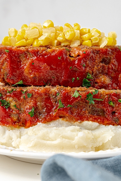 two slices of meatloaf over mashed potatoes topped with corn