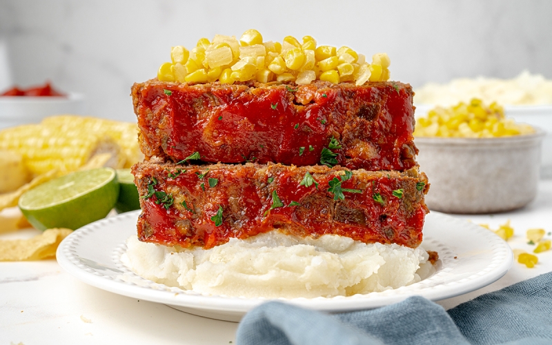 two slices of meatloaf over mashed potatoes topped with corn