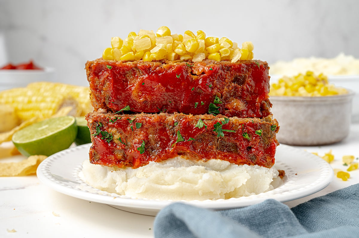 two slices of meatloaf over mashed potatoes topped with corn