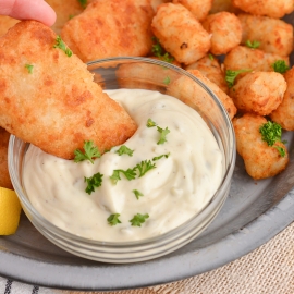 close up of battered fish dipping into tartar sauce