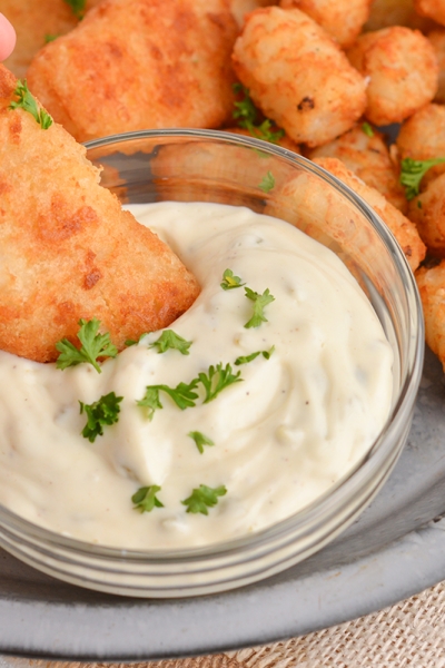 close up of battered fish dipping into tartar sauce