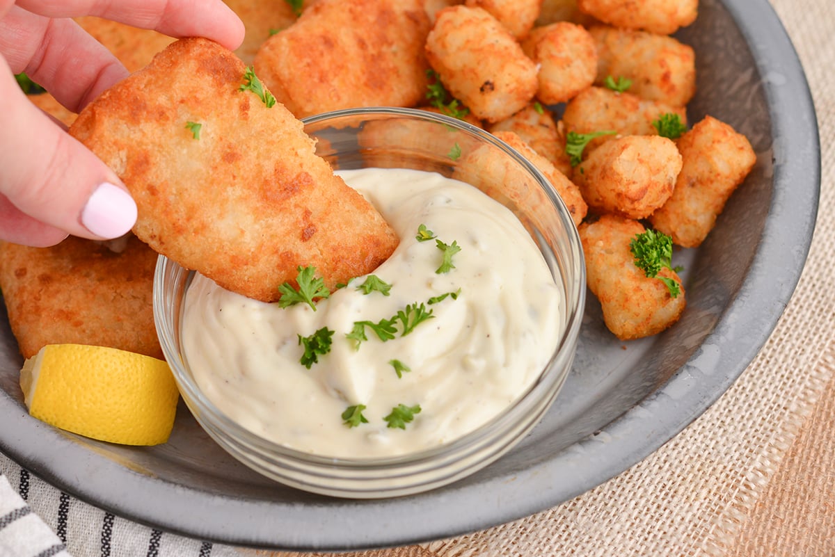 close up of battered fish dipping into tartar sauce