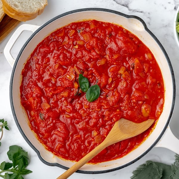 overhead shot of marinara in a pan with a wooden spoon