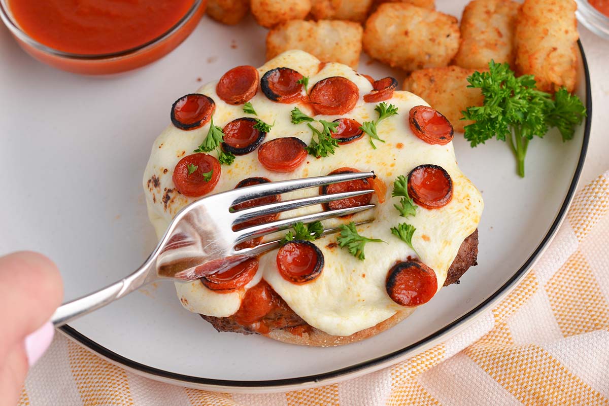 fork cutting into an open face pizza burger