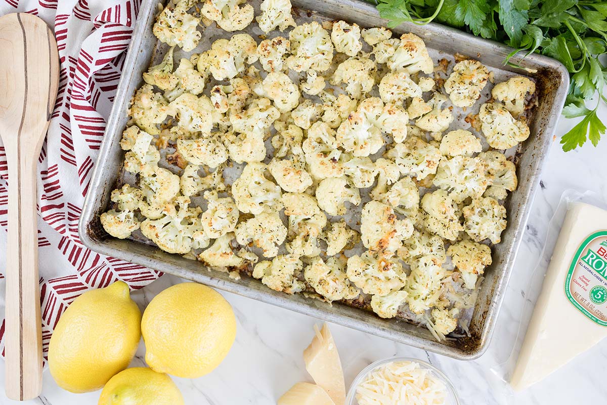 overhead of cauliflower roasted with parmesan cheese surrounding by lemons and wooden spoon 