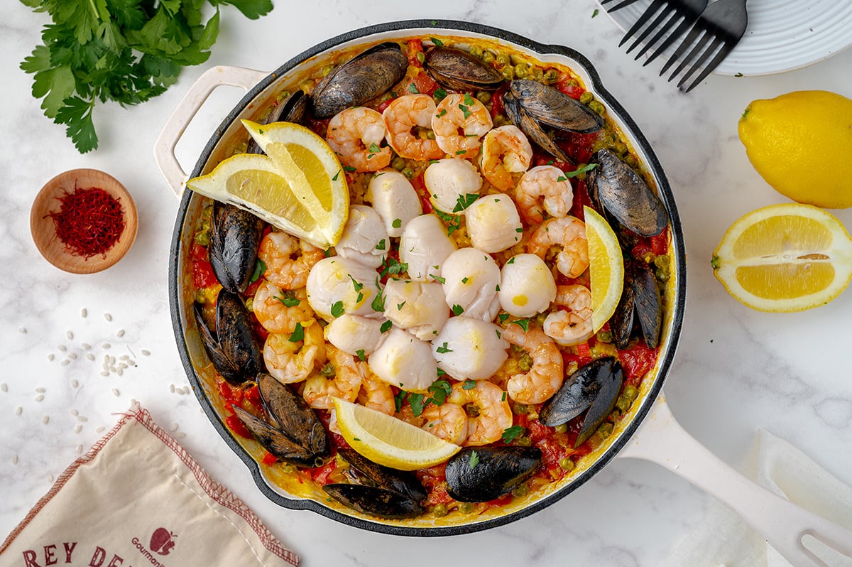 overhead of cooked paella in white pan with lemons and parsley 