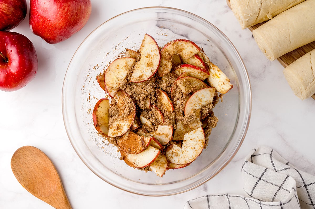 fresh apple slices tossed with brown sugar and cinnamon in a glass bowl 