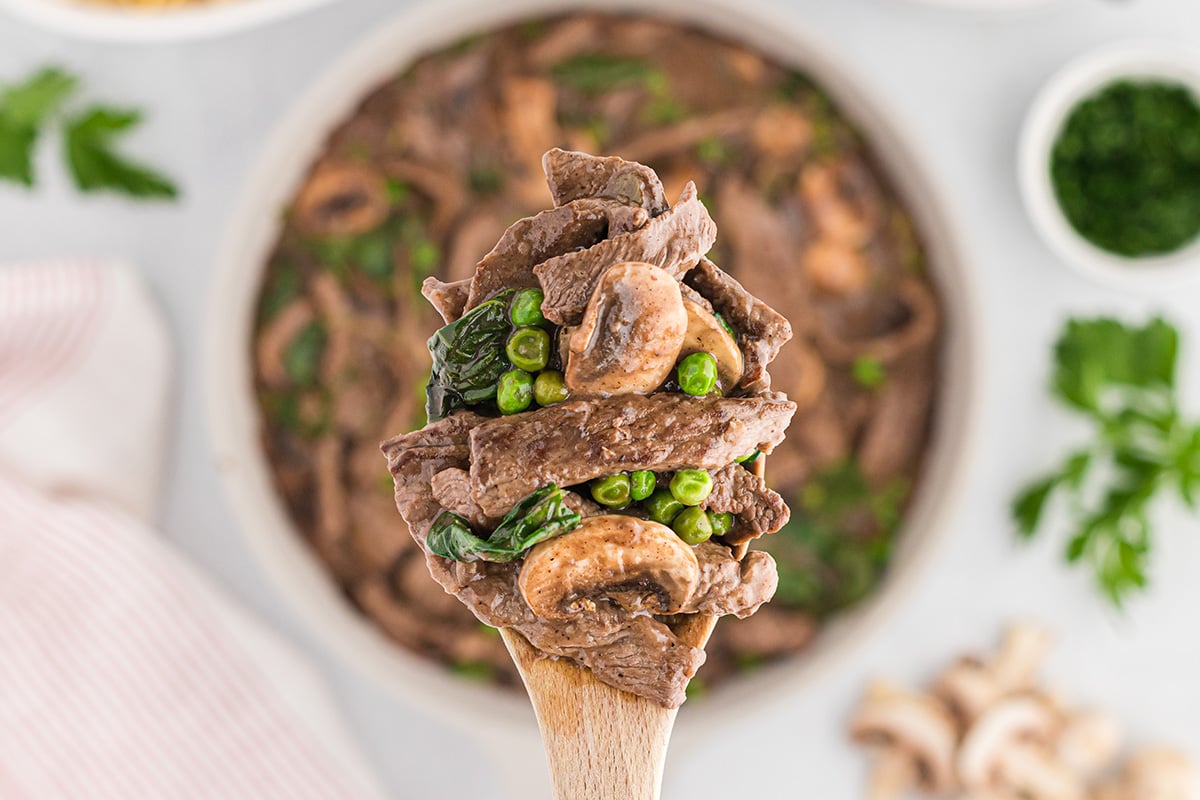 close up spoon of stroganoff with peas and spinach