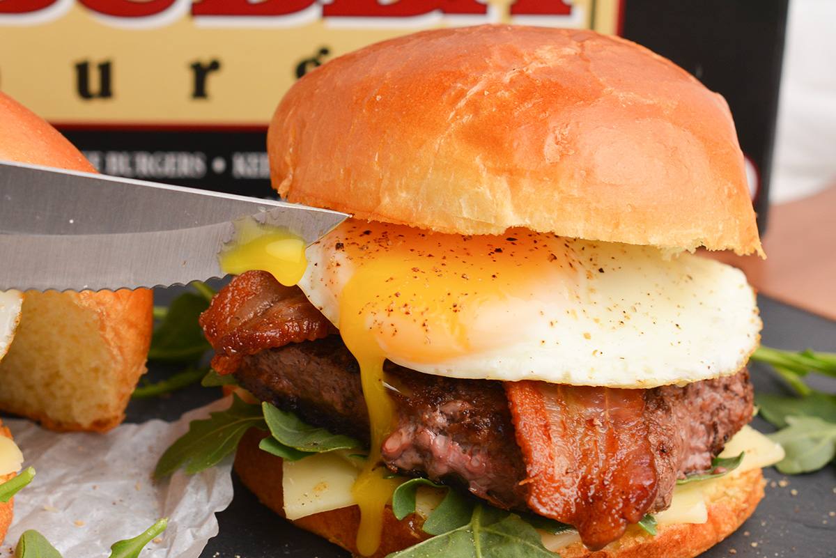 close up of a burger with a knife cutting through a runny yolk