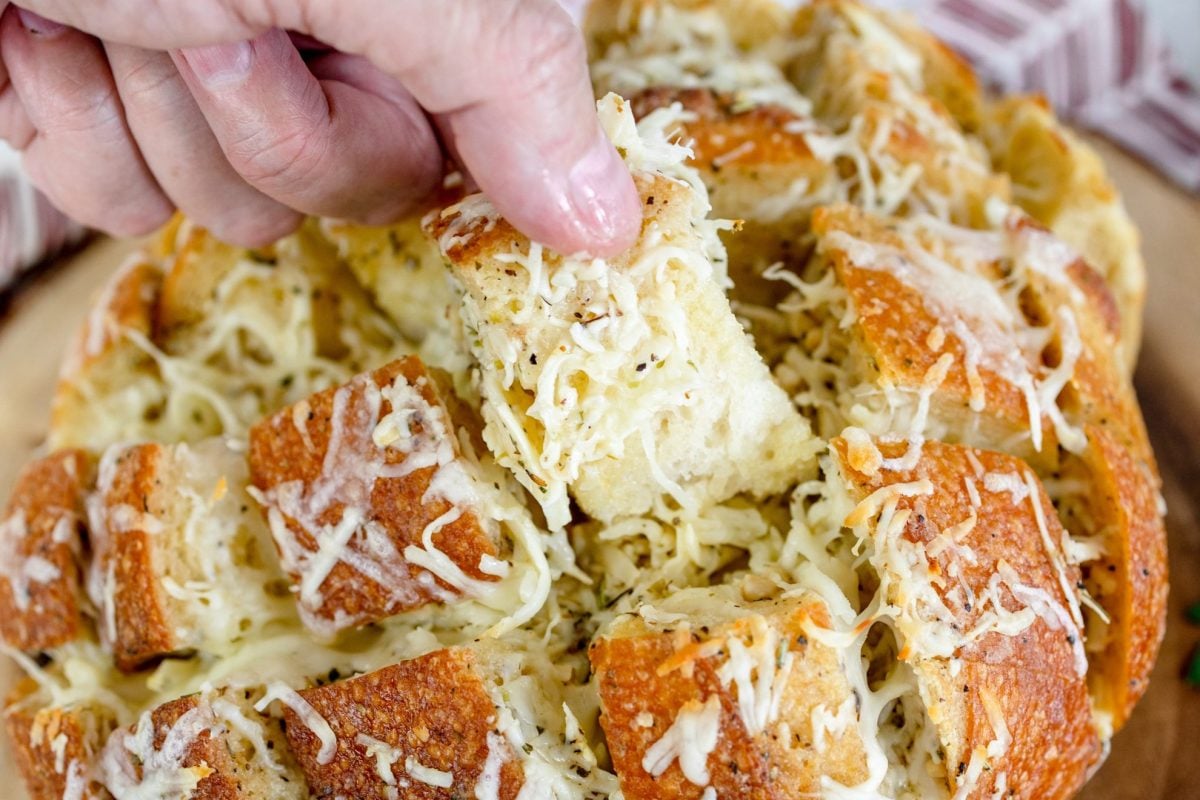 fingers pulling out a piece of cheesy garlic bread 