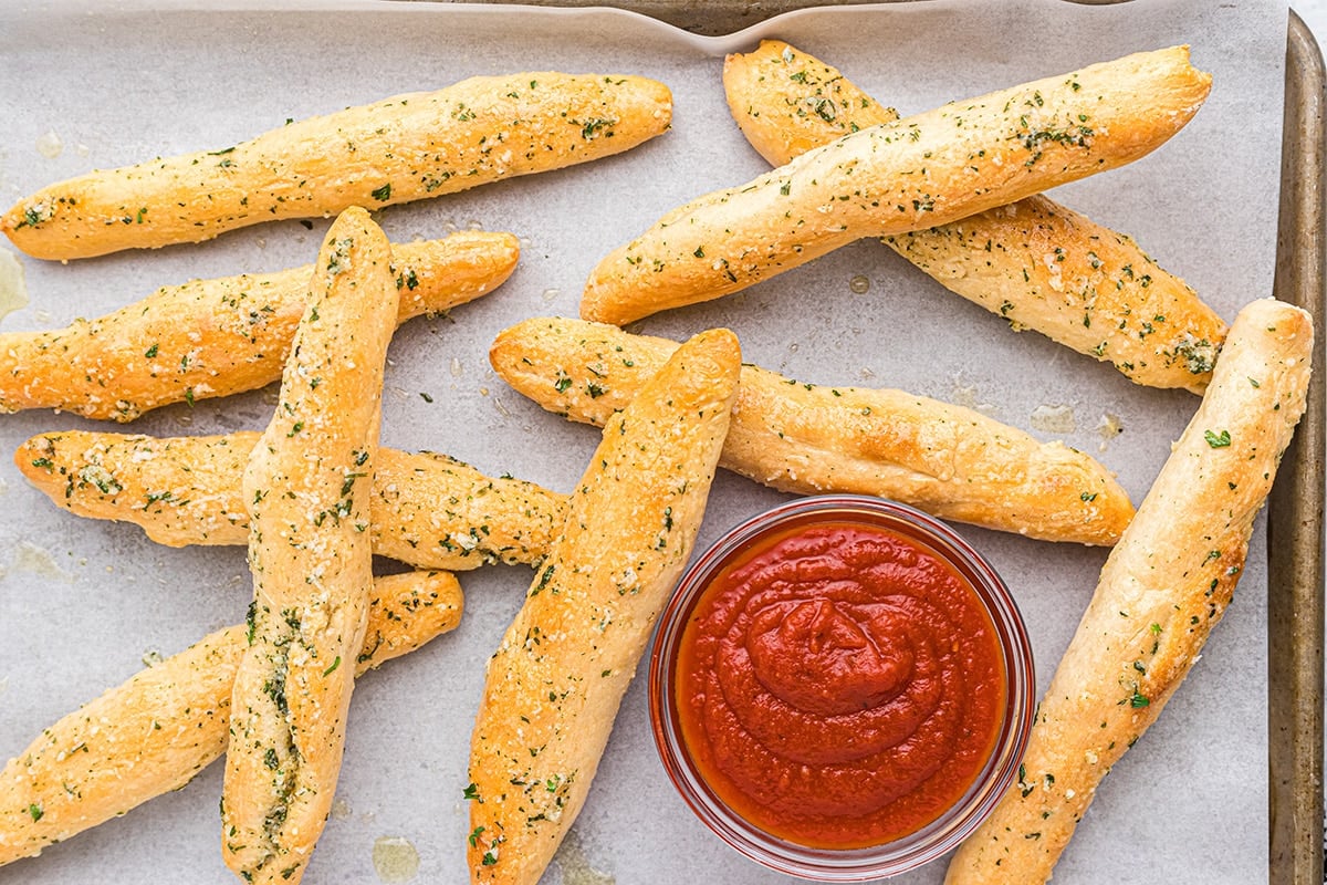 buttered garlic breadsticks on a baking sheet with marinara dipping sauce