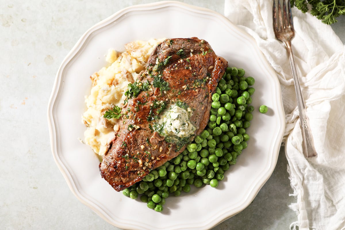 garlic butter sirlon steak on a plate with potatoes and peas